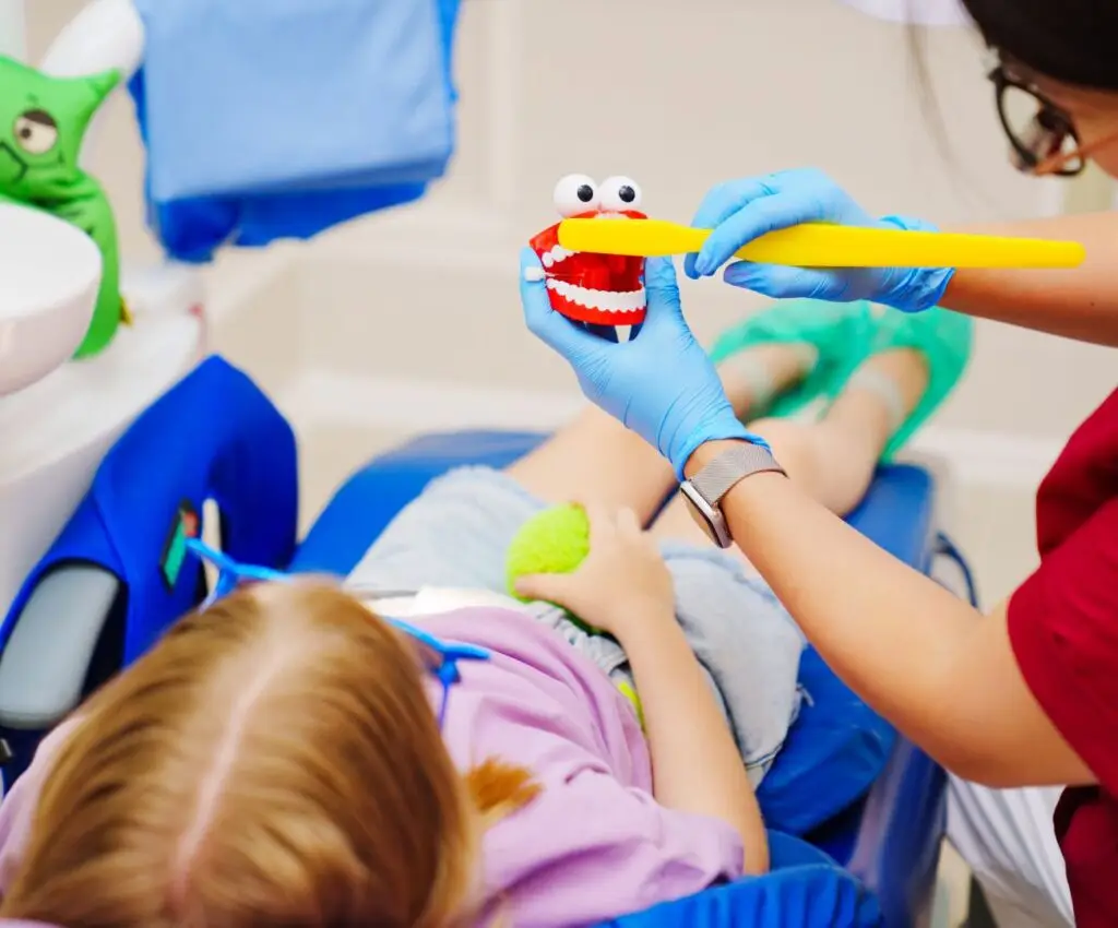 Odontopediatra sosteniendo modelo didactico de los dientes para enseñar las tecnicas de cepillado a un niño