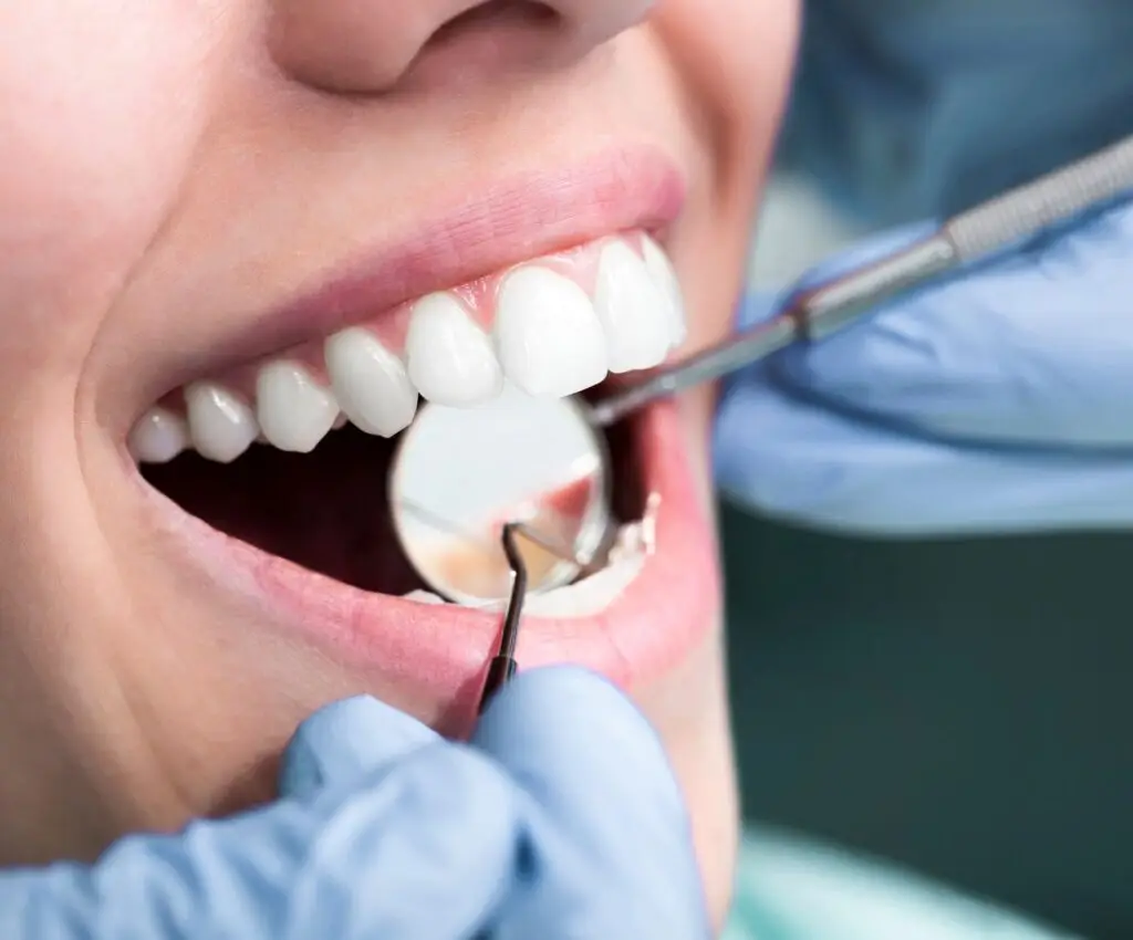 Odontolog revisando los dientes de una mujer adulta con espejo, pinza y explorador odontologico